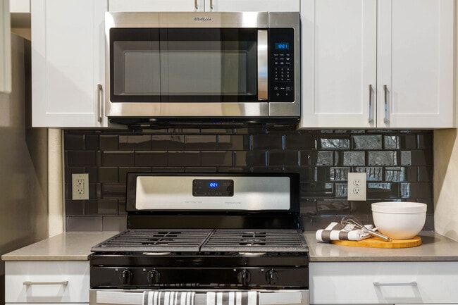 Renovated Package I kitchen with white cabinetry, grey quartz countertops, glass tile backsplash, and stainless steel appliances, and hard surface plank flooring