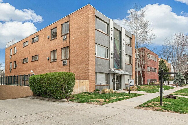 Inviting brick apartment building with modern facade and lush landscaping under a bright blue sky.